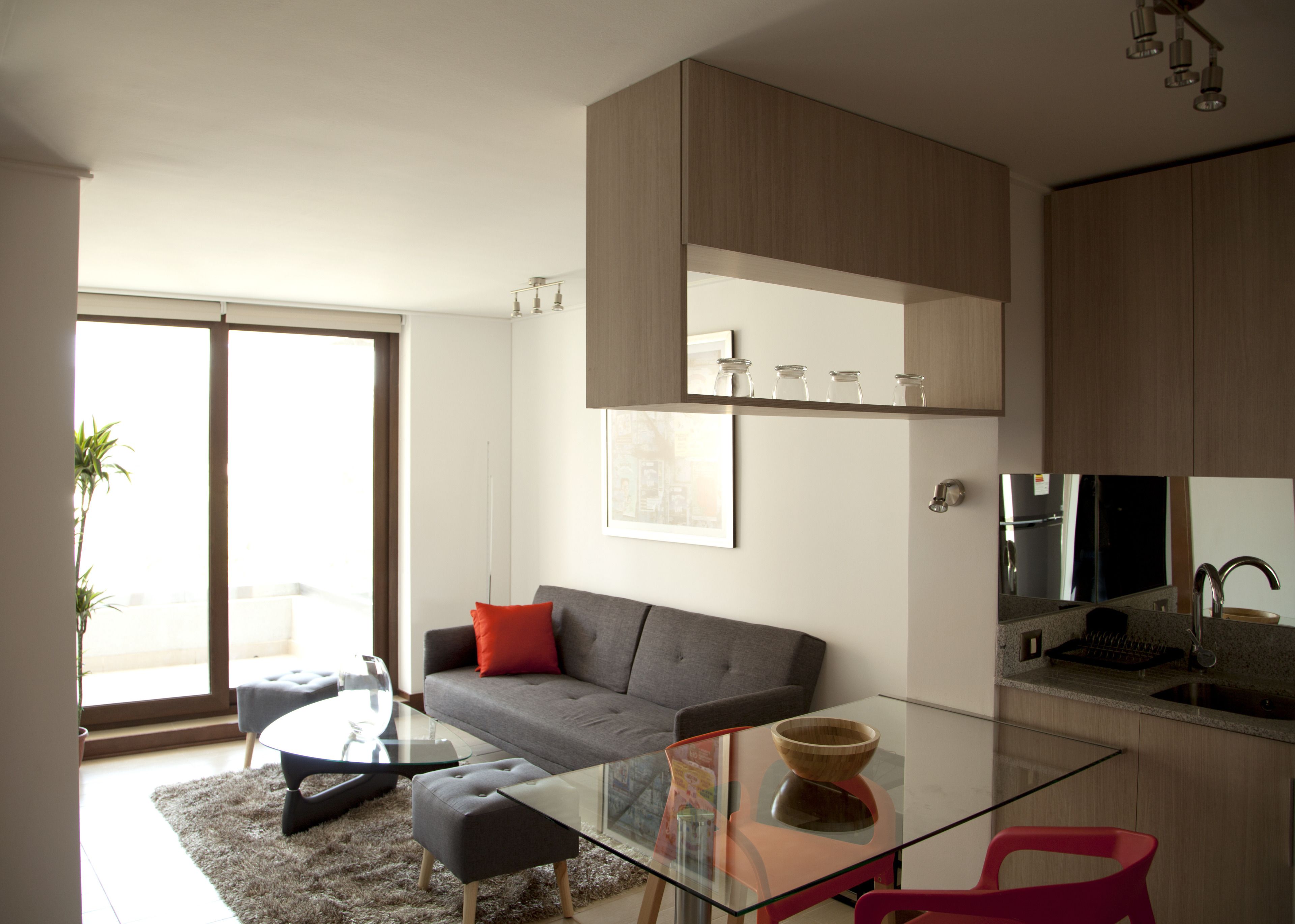 A modern living room with a glass coffee table, a grey sofa with a red pillow, and a glass dining table.