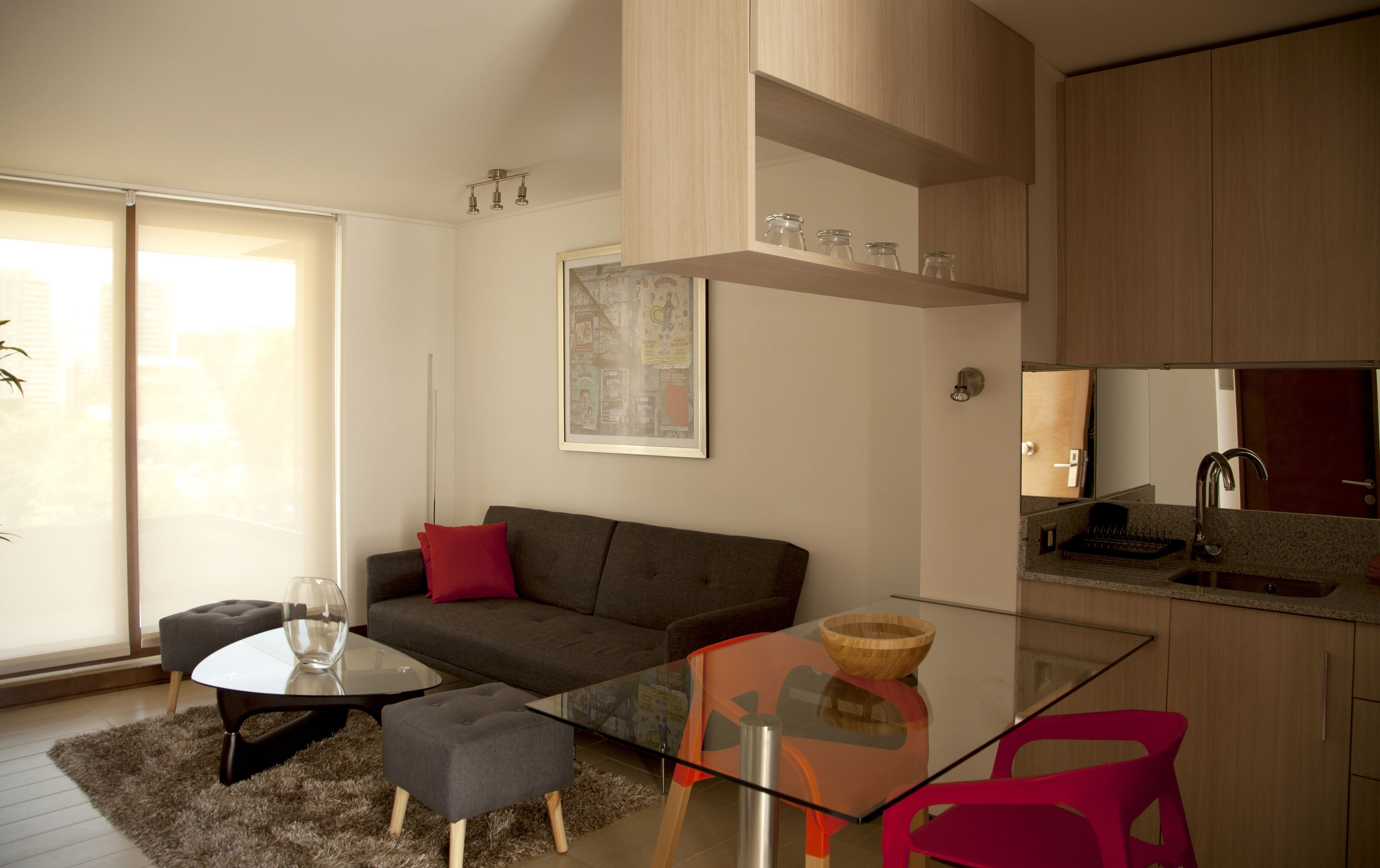 A modern living space with a glass dining table, grey sofa, and red chairs.