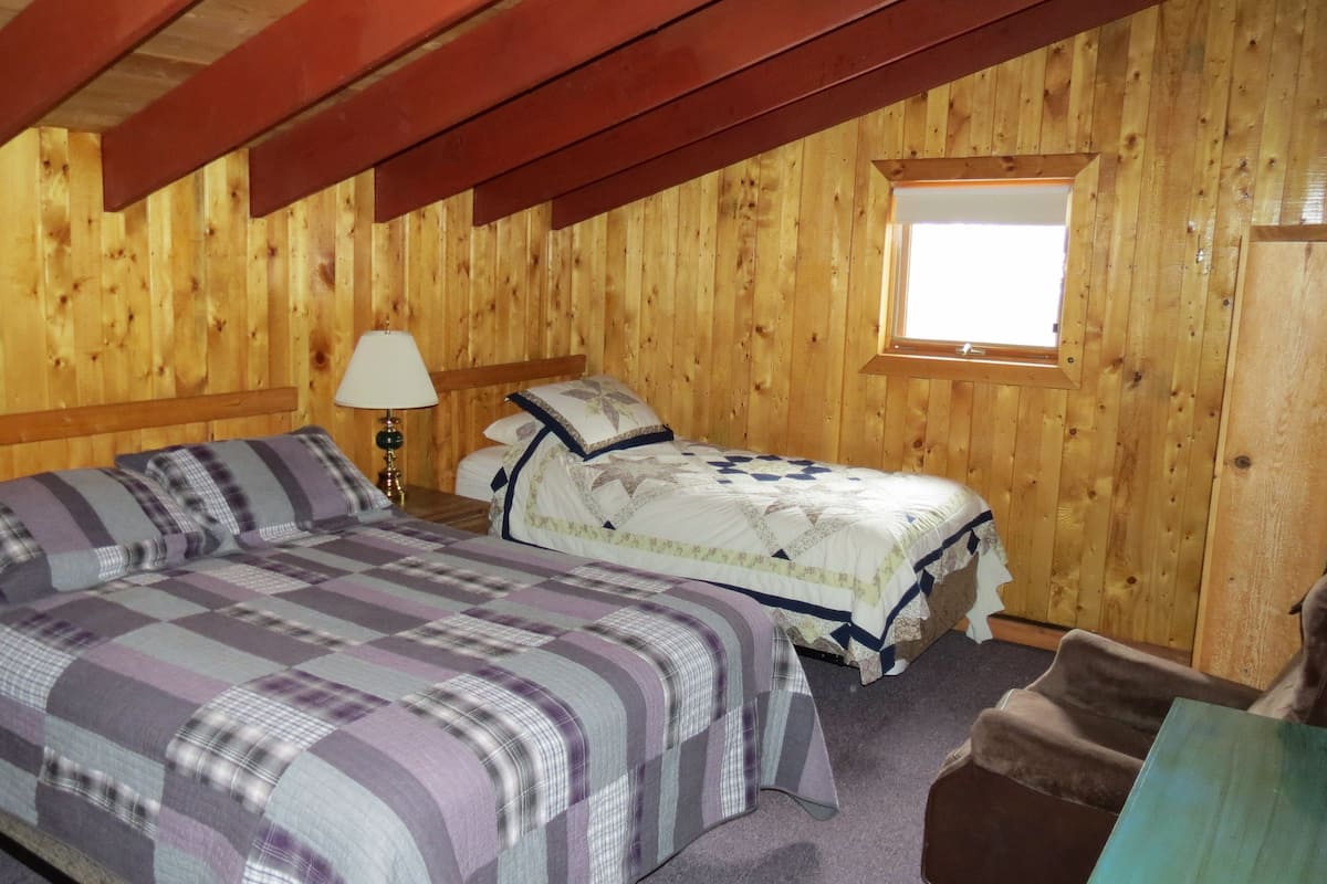 Quarto de cabana de madeira com cama, mesa de cabeceira, luminária e janela.