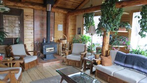 Un interior de cabaña acogedor con estufa de leña, muebles de madera y varias plantas.