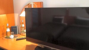 A television on a wooden surface with a remote control, a lamp, and a bottle of water. - Hotel The New Fox (Affligem)