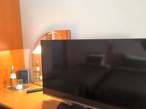 A television on a wooden surface with a remote control, a lamp, and a bottle of water. - Hotel The New Fox (Affligem)