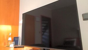 A flat-screen TV on a wooden surface, a bottle, a glass, and a small card. - Hotel The New Fox (Affligem)