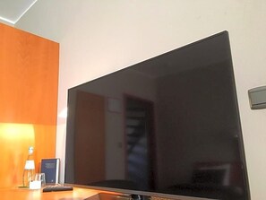 A flat-screen TV on a wooden surface, a bottle, a glass, and a small card. - Hotel The New Fox (Affligem)