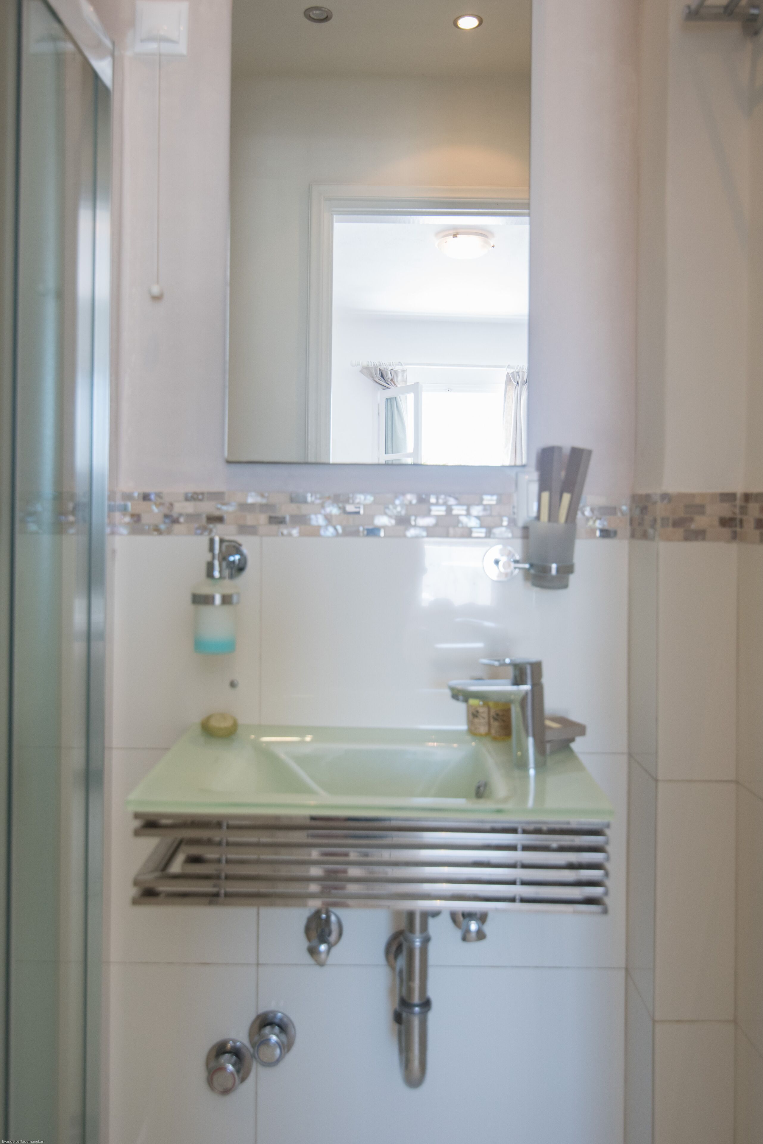 Un baño con lavamanos de vidrio, un espejo y zona de ducha.