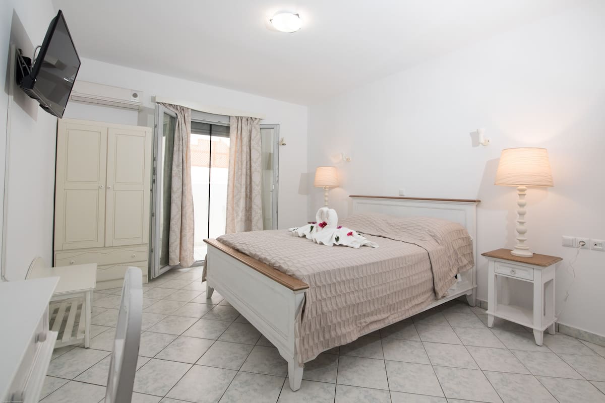 A bedroom with a bed, bedside tables, a TV mounted on the wall, and a door leading to a balcony.