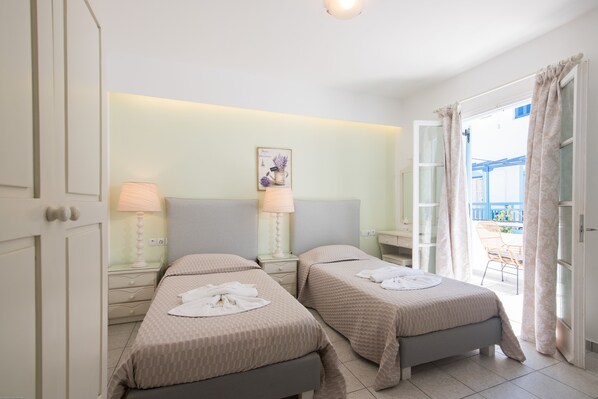 A hotel room with two beds, bedside lamps, a small table, a wall-mounted picture, and a balcony with a chair.