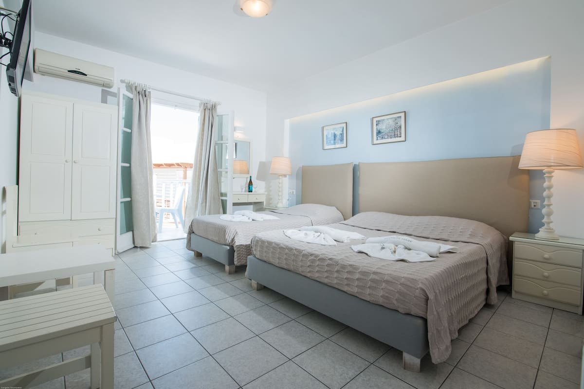 A hotel room with two beds, a desk, a chair, a wardrobe, and a bathroom visible through an open door.