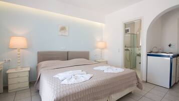 A hotel room with a bed, two bedside lamps, a small desk with a mirror, and a bathroom visible through an archway.