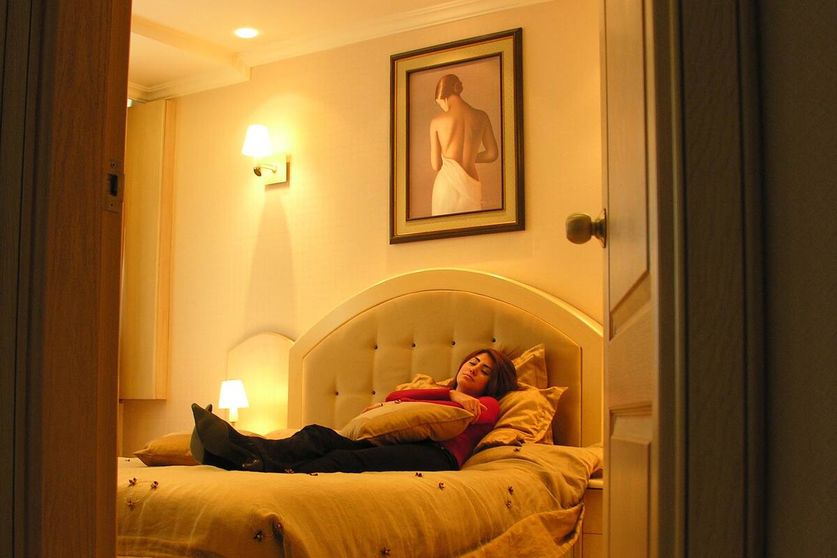 Quarto com cama, mesa de cabeceira, luminária na parede e quadro emoldurado.