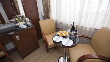 A hotel room with a dining area featuring a table set for two, a sofa, and a small kitchen area with a coffee maker and kettle.