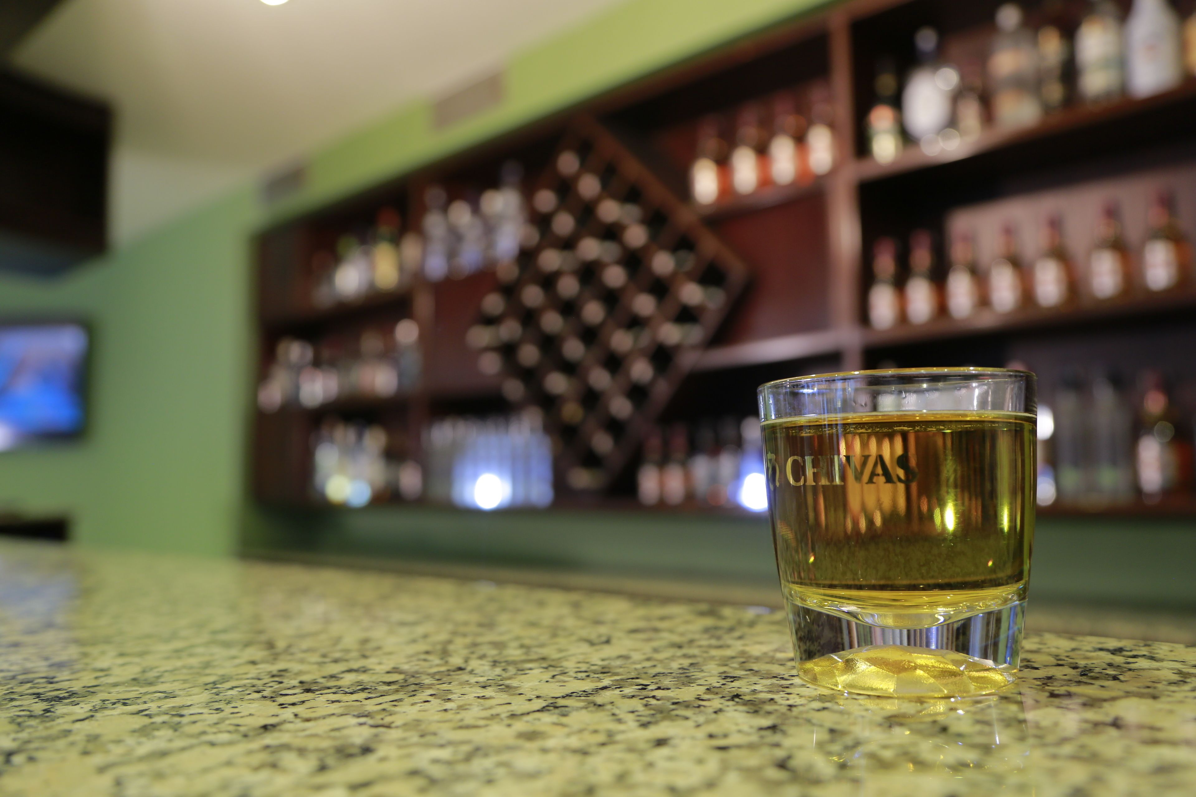 Ein Glas Whiskey auf einer Theke, im Hintergrund unscharf gestellte Regale und Flaschen.