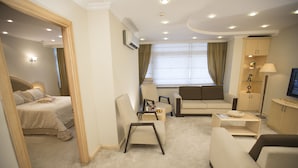 A hotel room with a bed, a sitting area with a sofa and armchairs, a small table, a cabinet, and a television. - Mersin Oteli (Mersin)