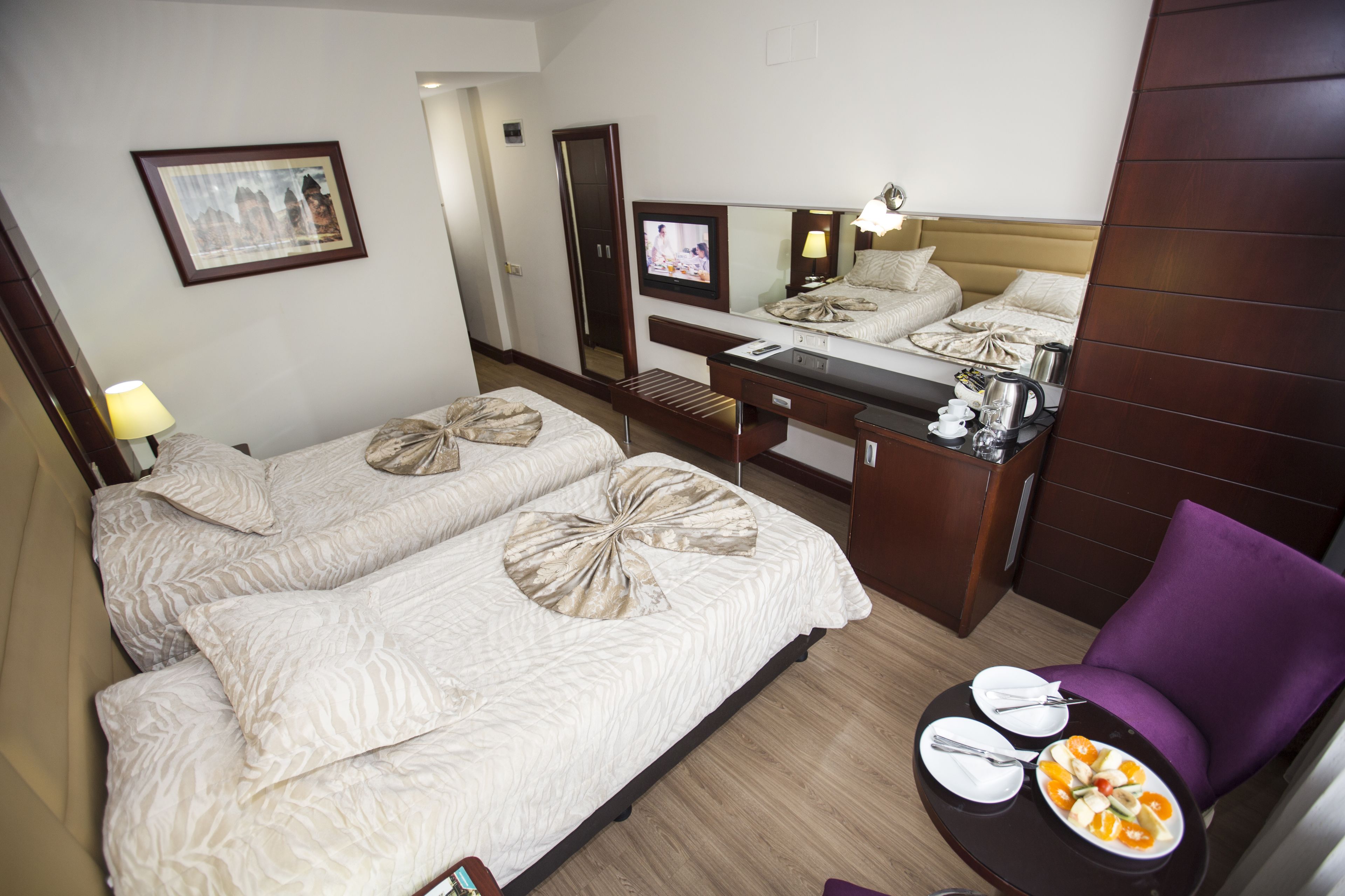 Habitación de hotel con dos camas, un escritorio y una silla, una mesa de comedor con platos y cubiertos, y un televisor.