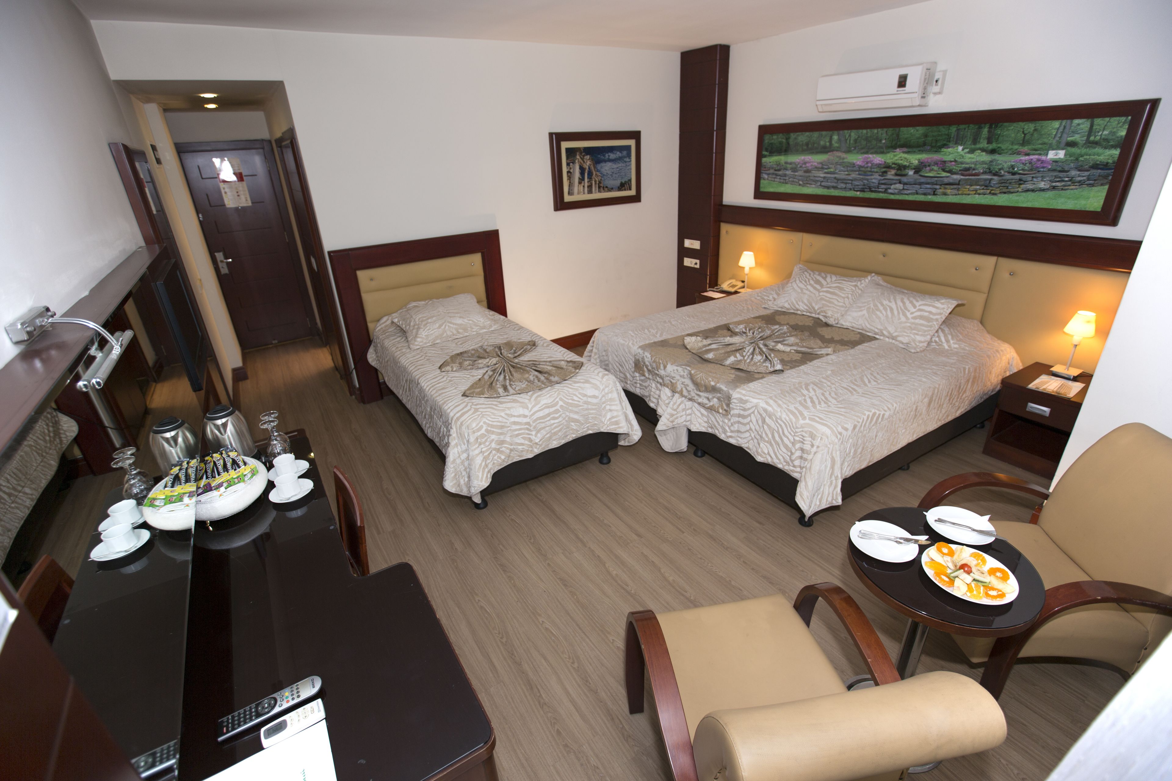 A hotel room with two beds, a dining table with plates and cutlery, a TV, and a painting on the wall.