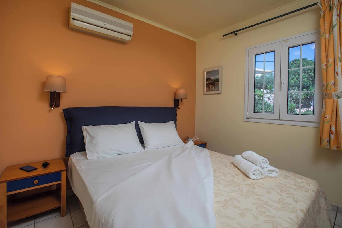 A neatly made bed with white linens, a blue headboard, and two wall-mounted lamps.
