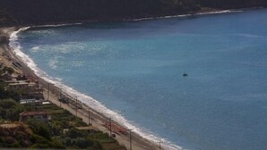 A coastal area with a beach, a small boat, and buildings along the shore. - Garbis Villas (Kefalonia)