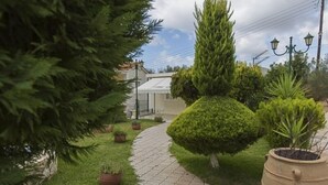 A paved pathway leading to a building with a white facade and a green roof. - Garbis Villas (Kefalonia)