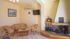 A living room with a sofa, chairs, a small table with fruit, a television, and a fireplace with decorative items. - Garbis Villas (Kefalonia)