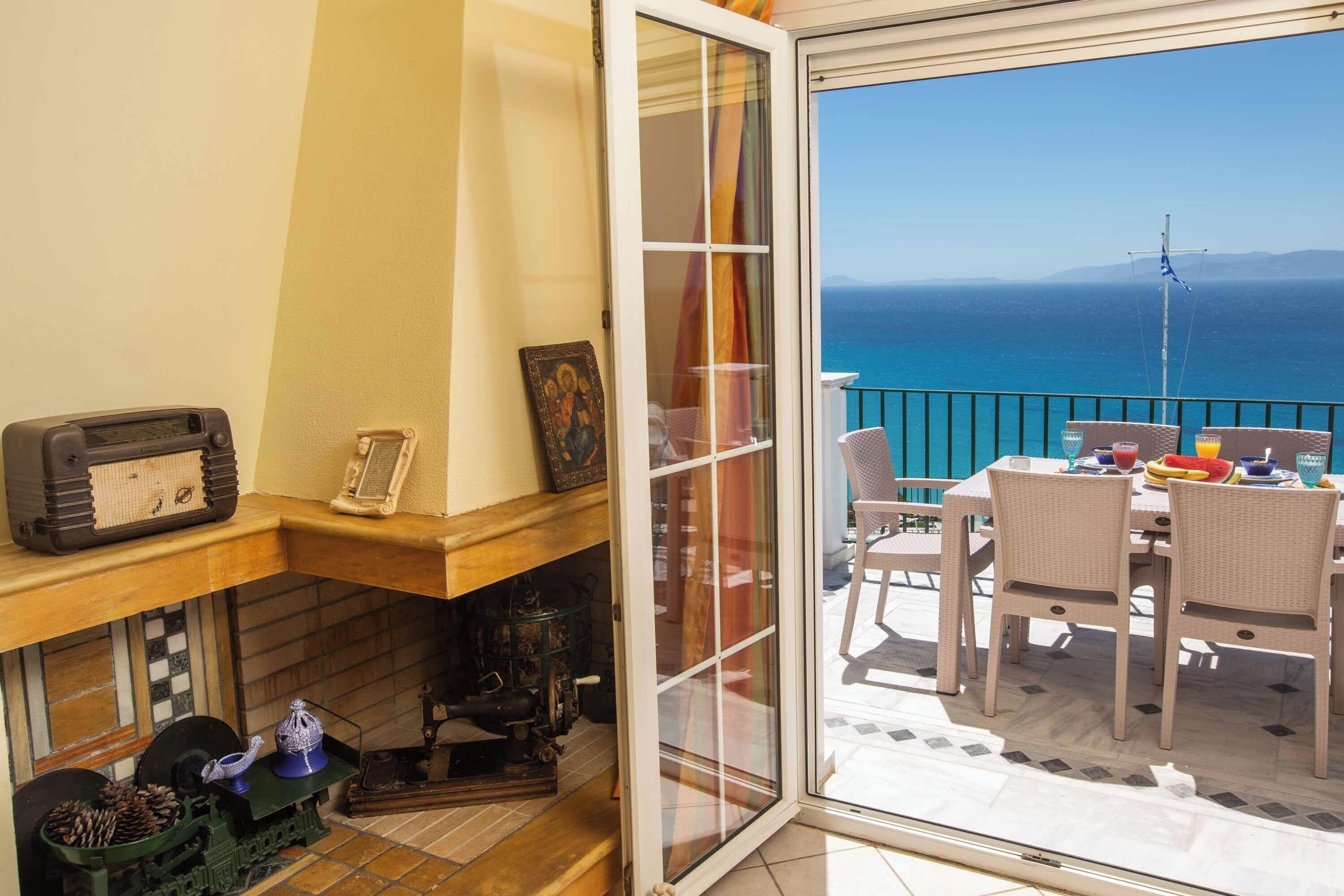 Een balkon met een tafel en stoelen, een uitzicht op zee, en een houten plank met verschillende spullen.