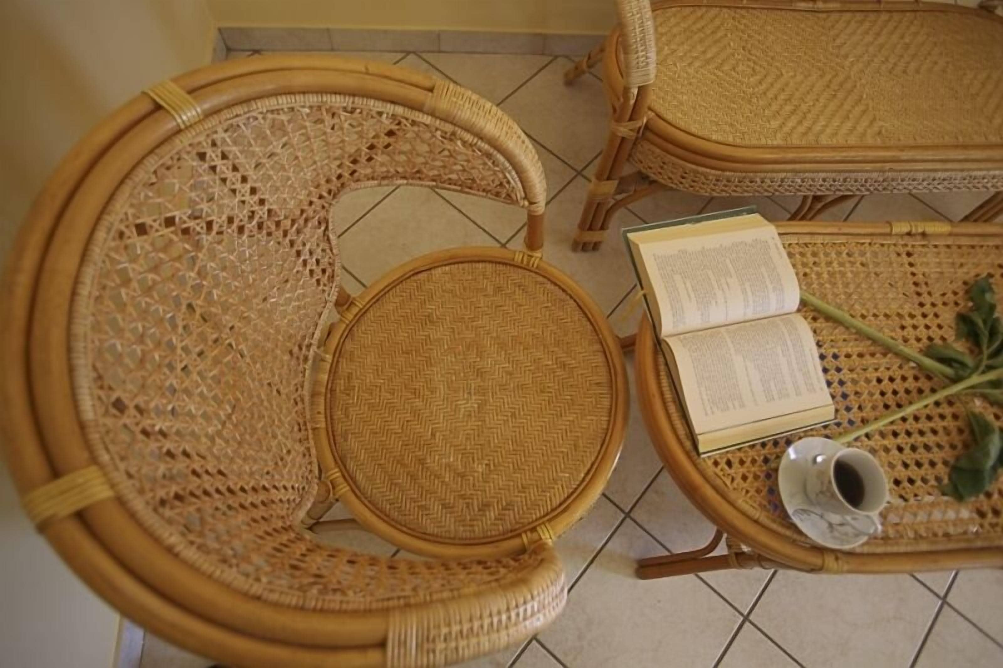 Ein Korbsessel und ein Tisch mit einem Buch und einer Tasse auf einem Fliesenboden.