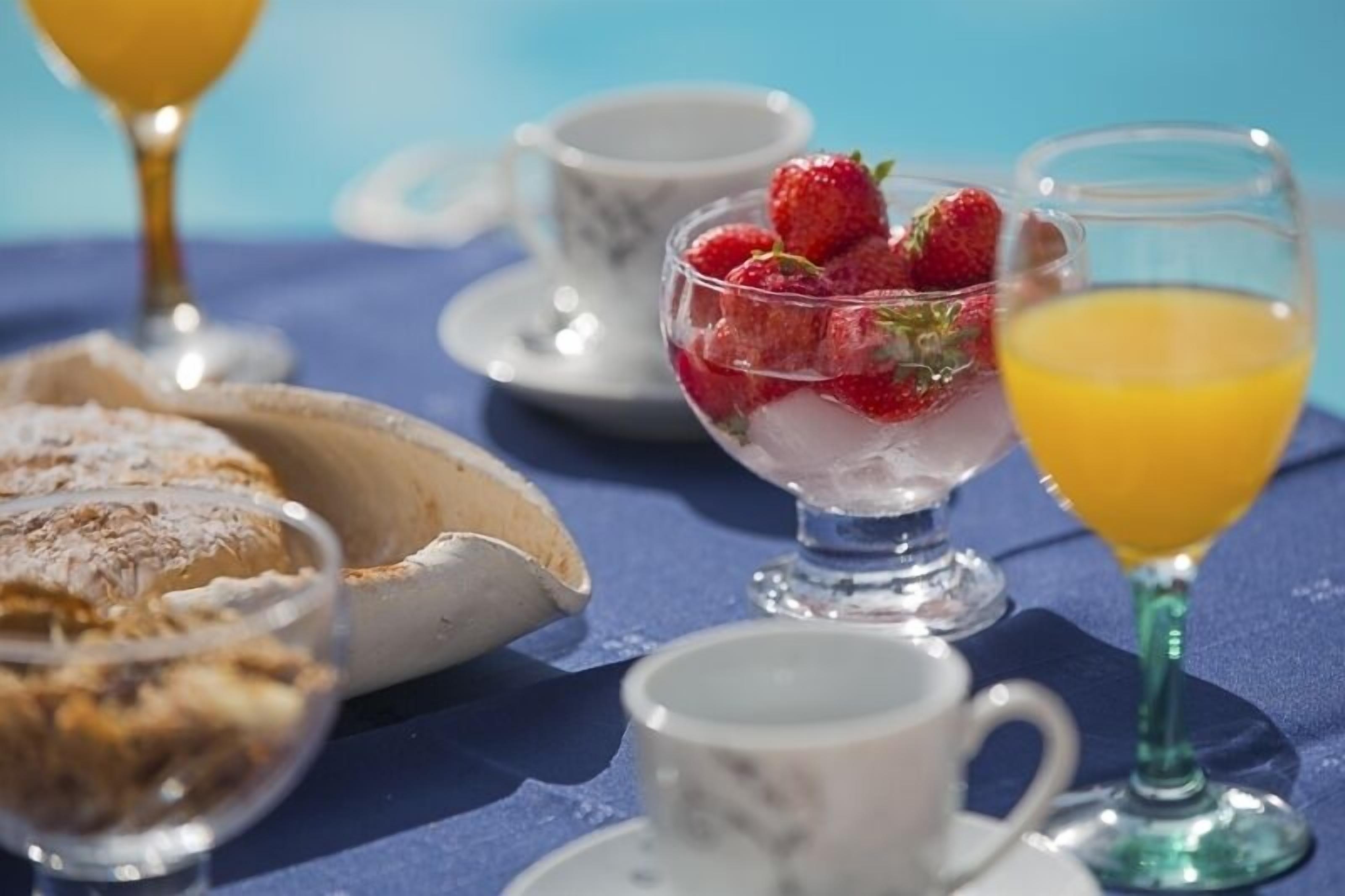 Un desayuno con un tazón de fresas, un vaso de jugo de naranja y una taza de té sobre un mantel azul.