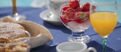 Un desayuno con un tazón de fresas, un vaso de jugo de naranja y una taza de té sobre un mantel azul.