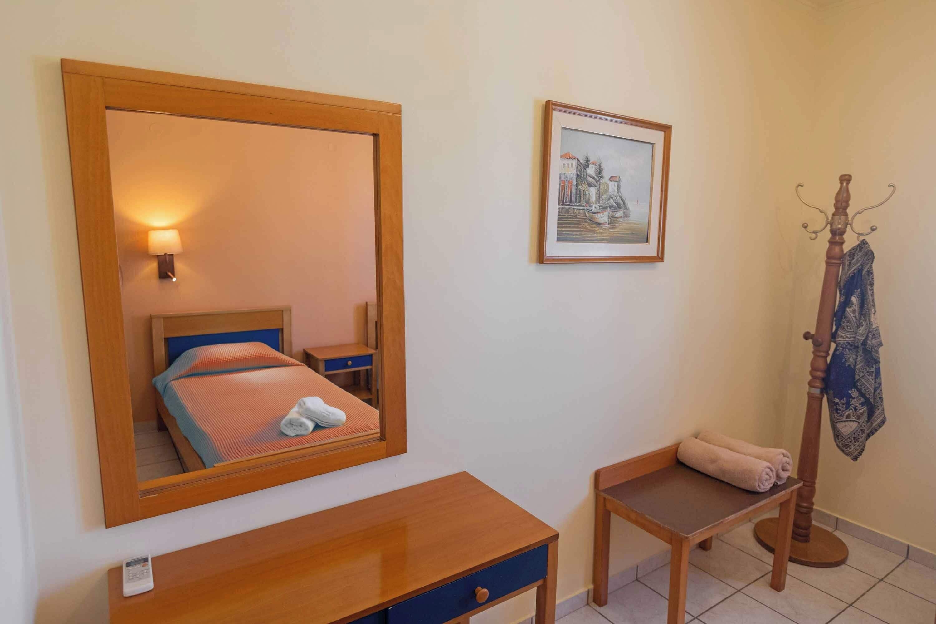 Ein Schlafzimmer mit einem großen Spiegel, einem Nachttisch, einem Sessel, einem Kleiderständer und einem gerahmten Bild an der Wand.
