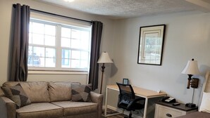 Una habitación de hotel con sofá, escritorio, silla, cama y ventana con cortinas.
