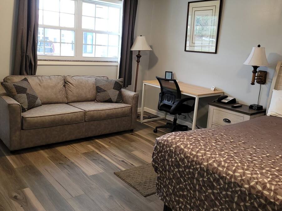 Une chambre d’hôtel avec un canapé, un bureau et une chaise, un lit et une fenêtre avec des rideaux.
