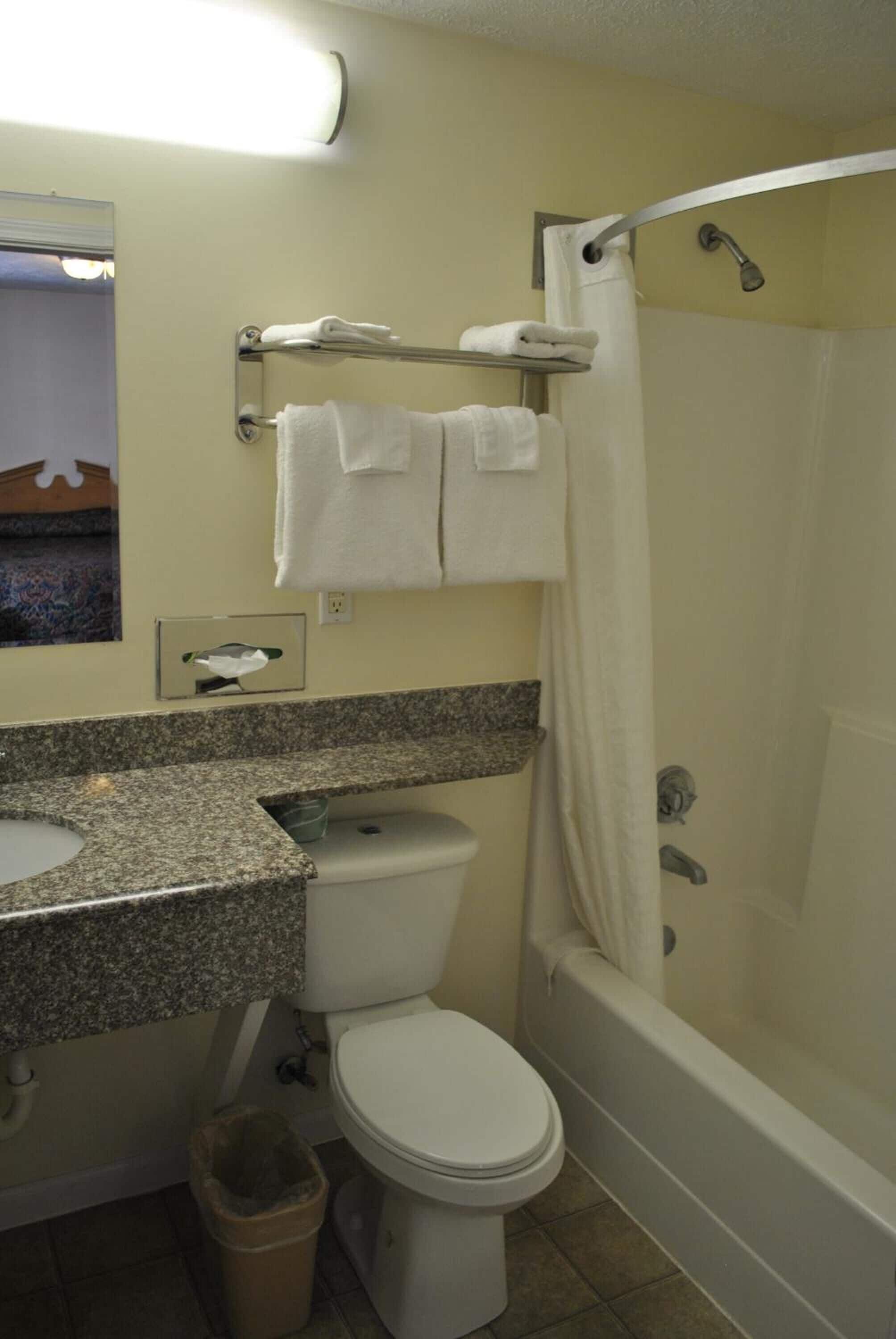 A bathroom with a toilet, sink, and bathtub. There are towels hanging on a rack above the toilet and a shower curtain.