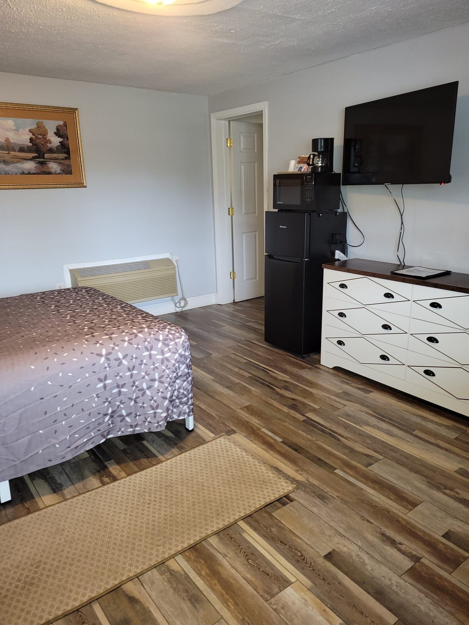 A bedroom with a bed, a dresser, a television, a refrigerator, and a door.