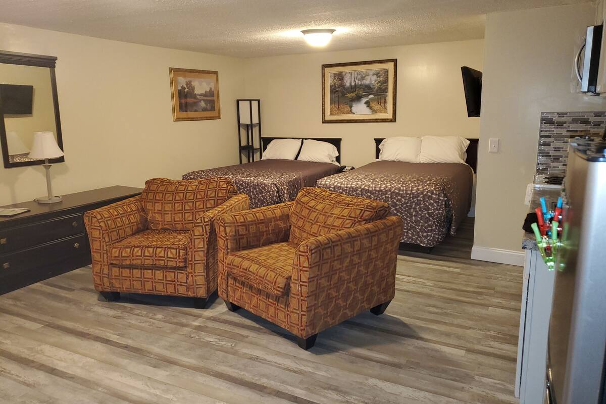 A hotel room with two beds, a dresser, a mirror, and two patterned armchairs.