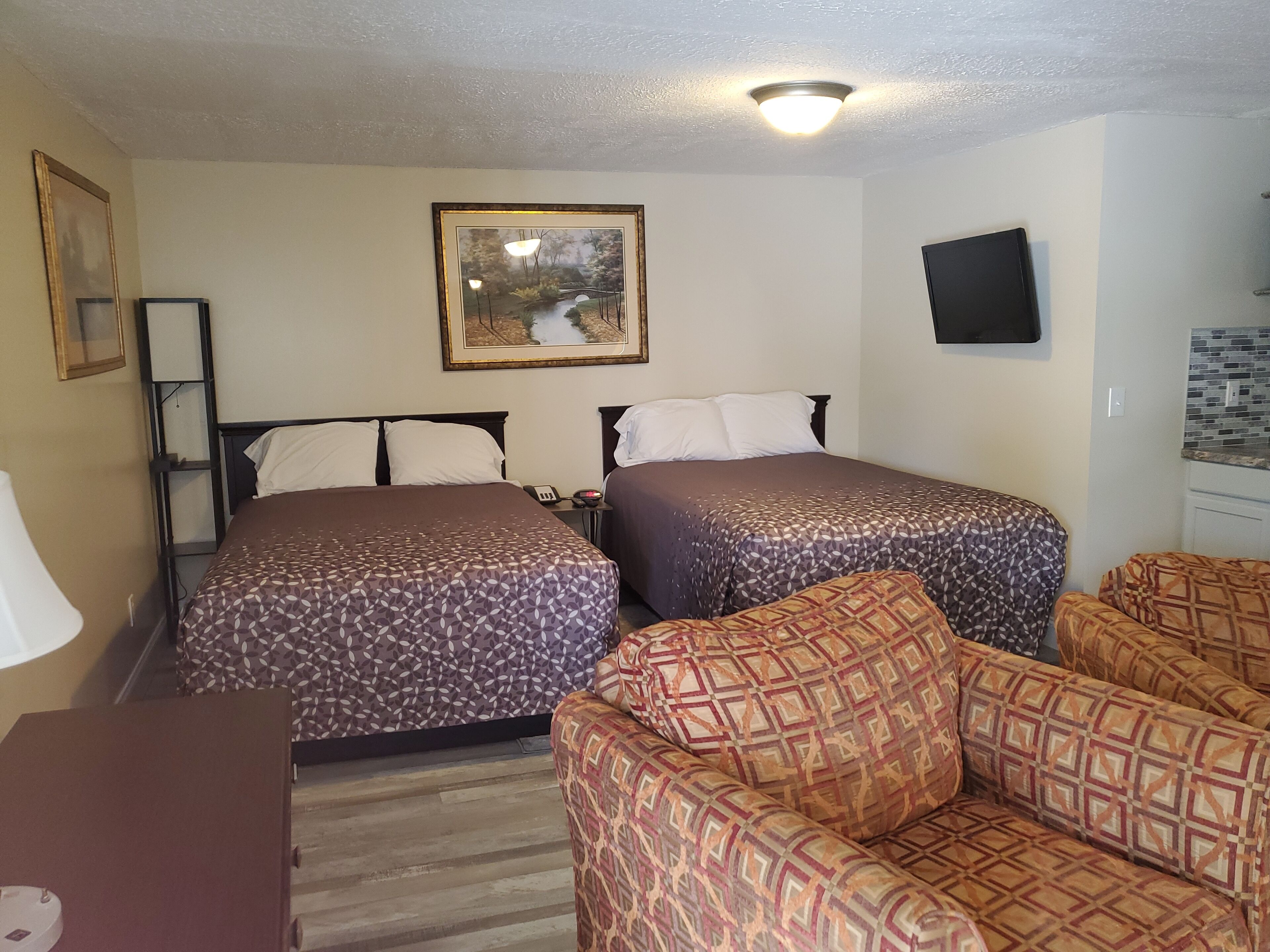 Habitación de hotel con dos camas, un sofá, un escritorio, una lámpara, un cuadro y un televisor en la pared.