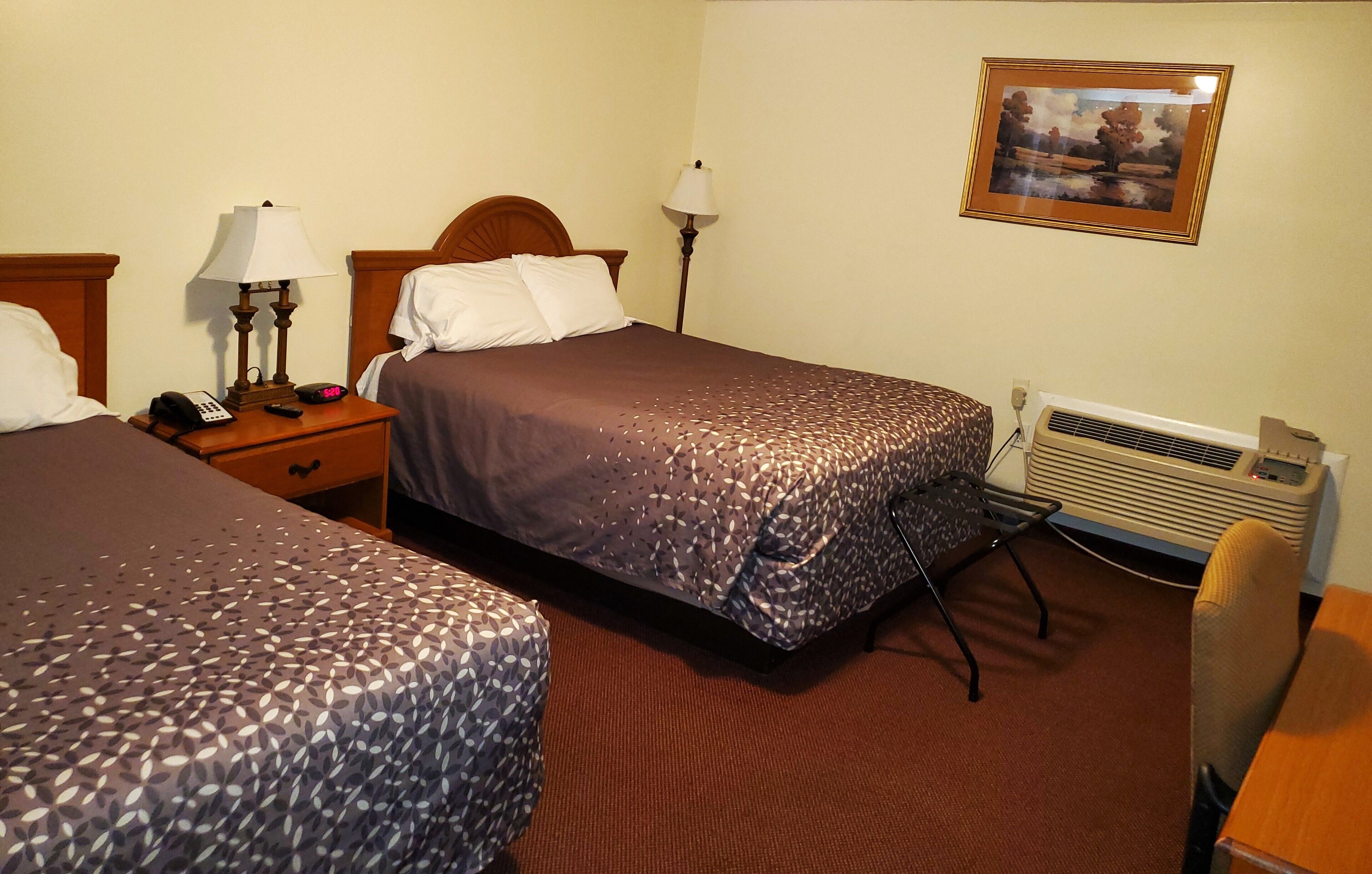 Habitación de hotel con dos camas, lámparas de noche, teléfono, aire acondicionado y un cuadro en la pared.