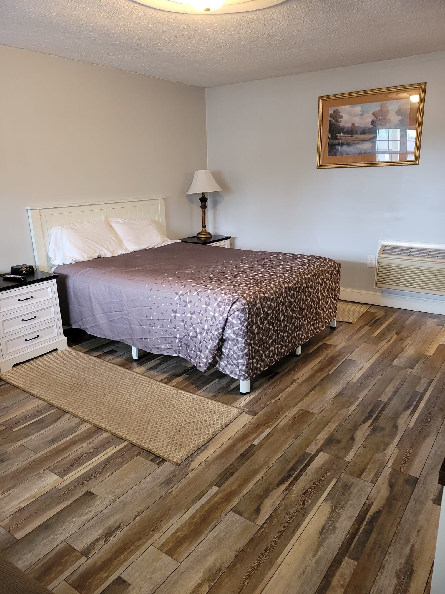 A bedroom with a bed, bedside table, lamp, and a painting on the wall.