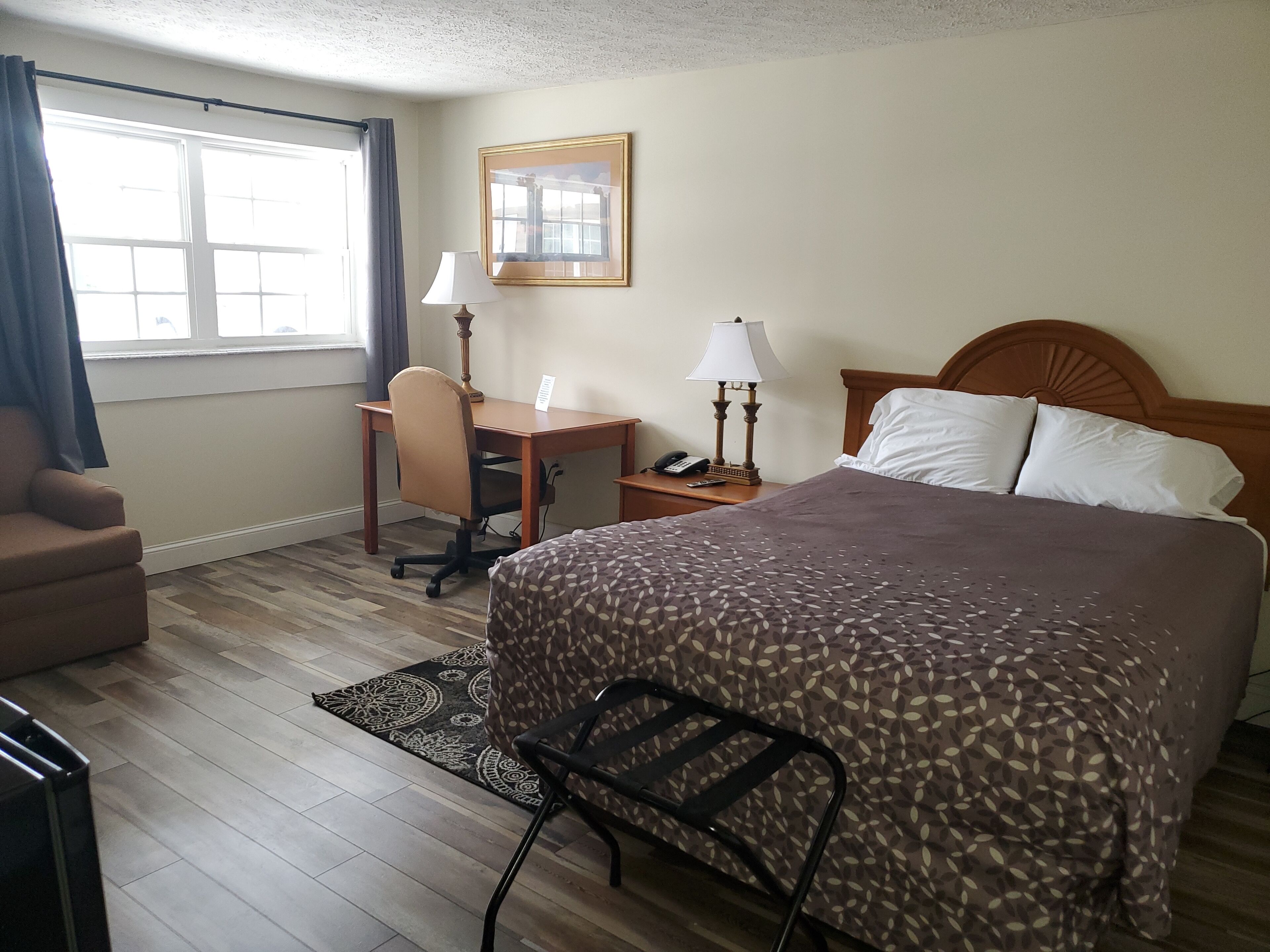 Habitación de hotel con cama, escritorio, silla, mesita de noche, lámpara, teléfono y ventana con cortinas.