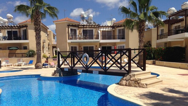 A swimming pool with a lifeguard station, lounge chairs, and palm trees. - Sirena Sunrise (Paphos)