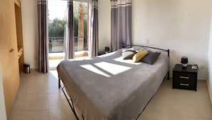 A bedroom with a bed, a nightstand, a lamp, and a view of the outdoors. - Sirena Sunrise (Paphos)