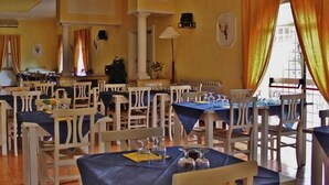 A dining area with multiple tables and chairs, yellow walls, and a large window with curtains. - Agriturismo Marco Simone (Rome)