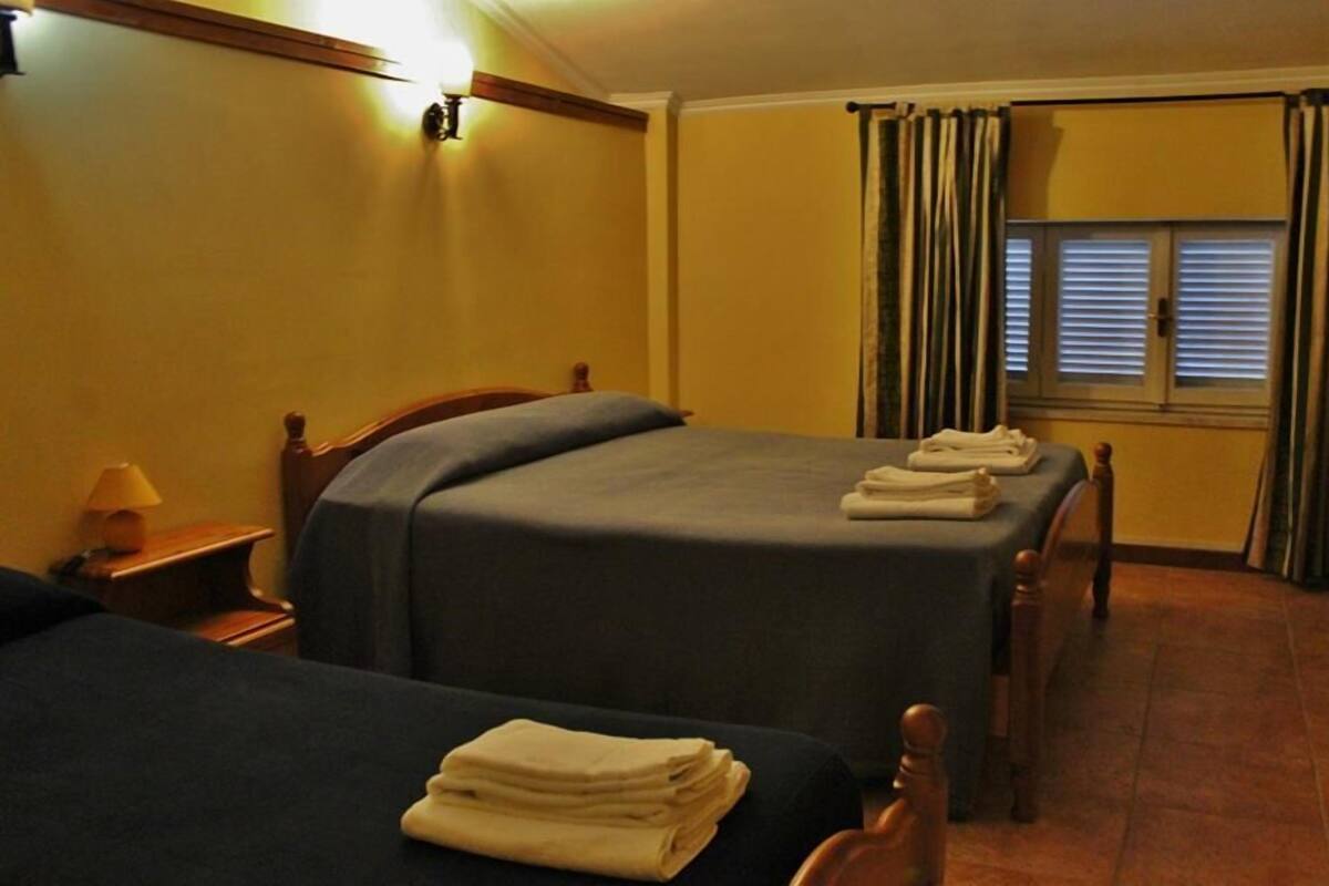 Une chambre d’hôtel avec deux lits, une table de chevet avec une lampe et une fenêtre avec des rideaux.