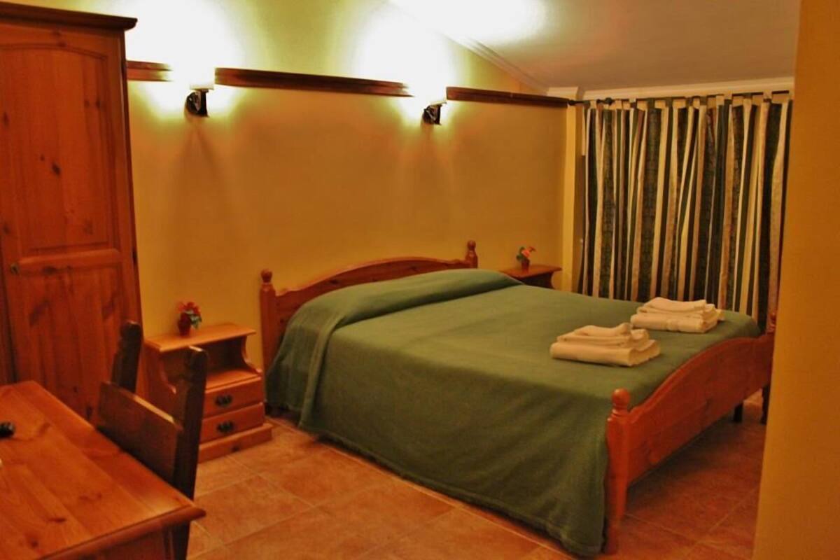Une chambre à coucher avec un lit en bois, une couvre-lit verte et une armoire en bois.