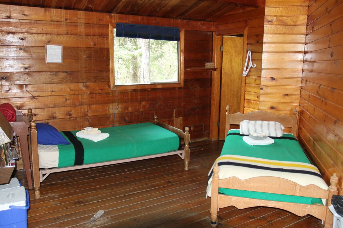 Une cabane avec deux lits en bois, une fenêtre et une porte.