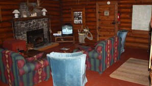 Interno di una baita in legno con camino in pietra, televisione e mobili a quadri.