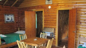 Una baita in legno con un tavolo da pranzo, sedie, un letto e angolo cottura.