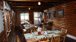 Una baita rustica in legno con diversi tavoli e sedie, un soffitto in legno e una porta che dà sull'esterno.