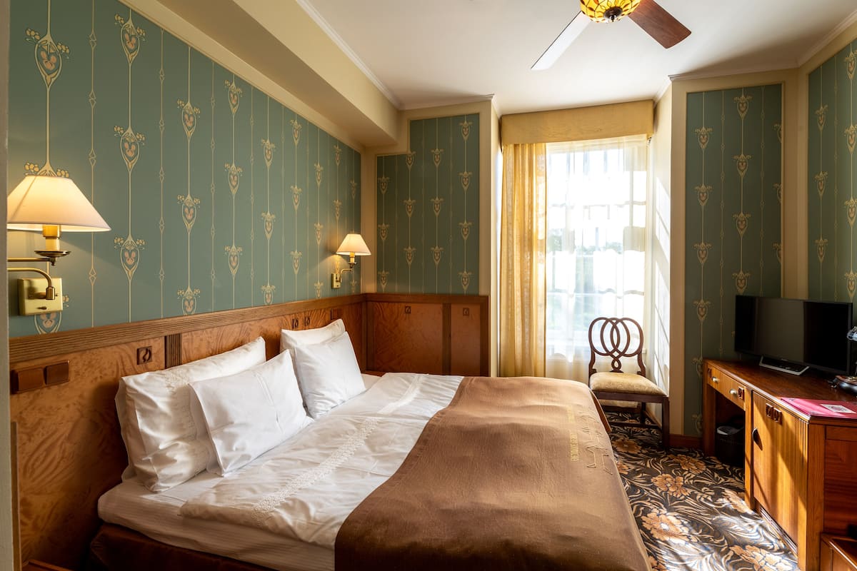 A hotel room with a large bed, two bedside lamps, a wooden headboard, a desk with a television, and a chair.