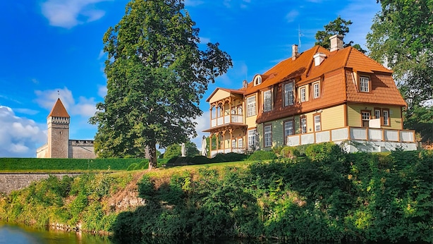 A historic building with a tower, a large tree, and a river. - Ekesparre Boutique Hotel (Kuressaare)