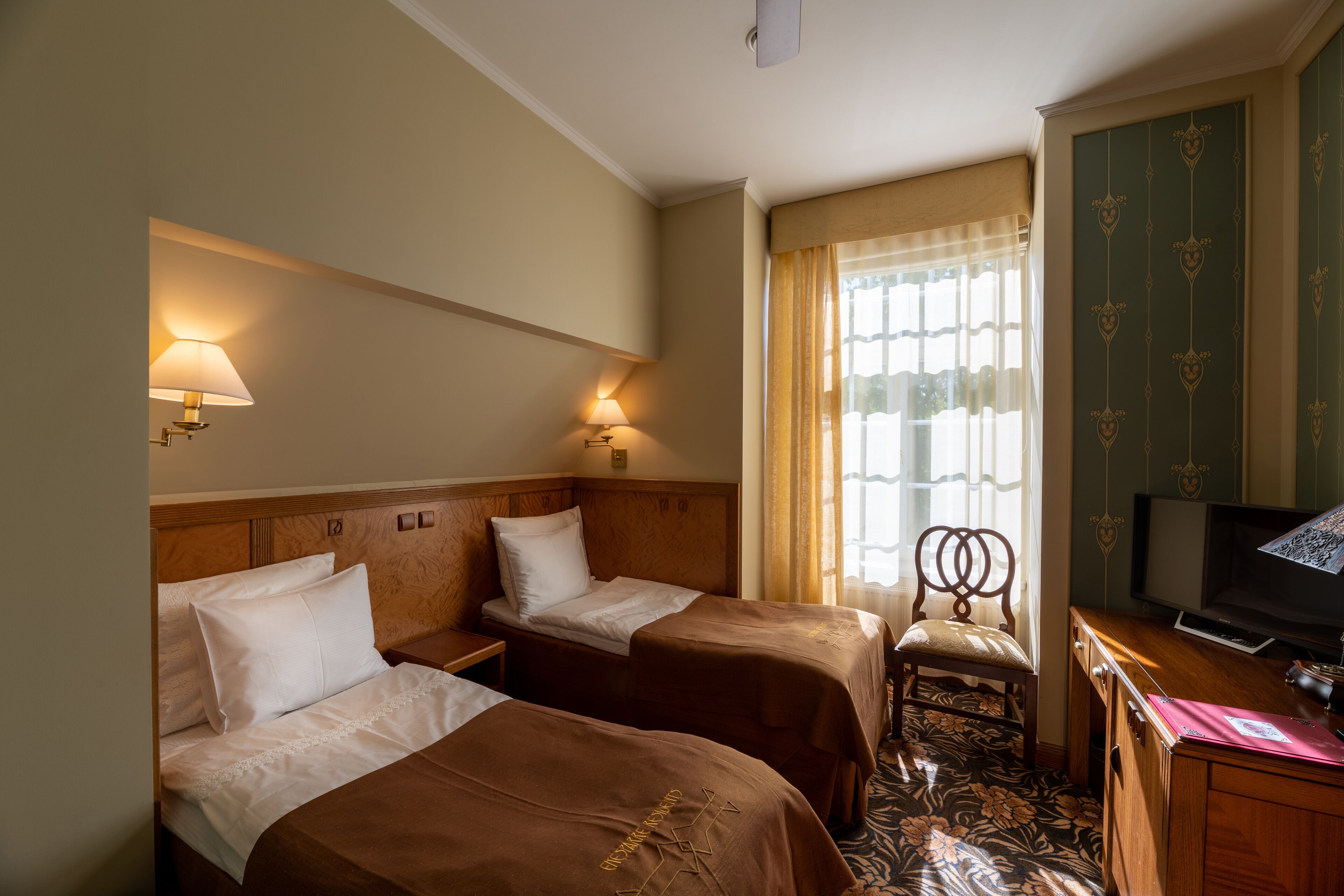A hotel room with two beds, a desk, a chair, a television, and a window with curtains.