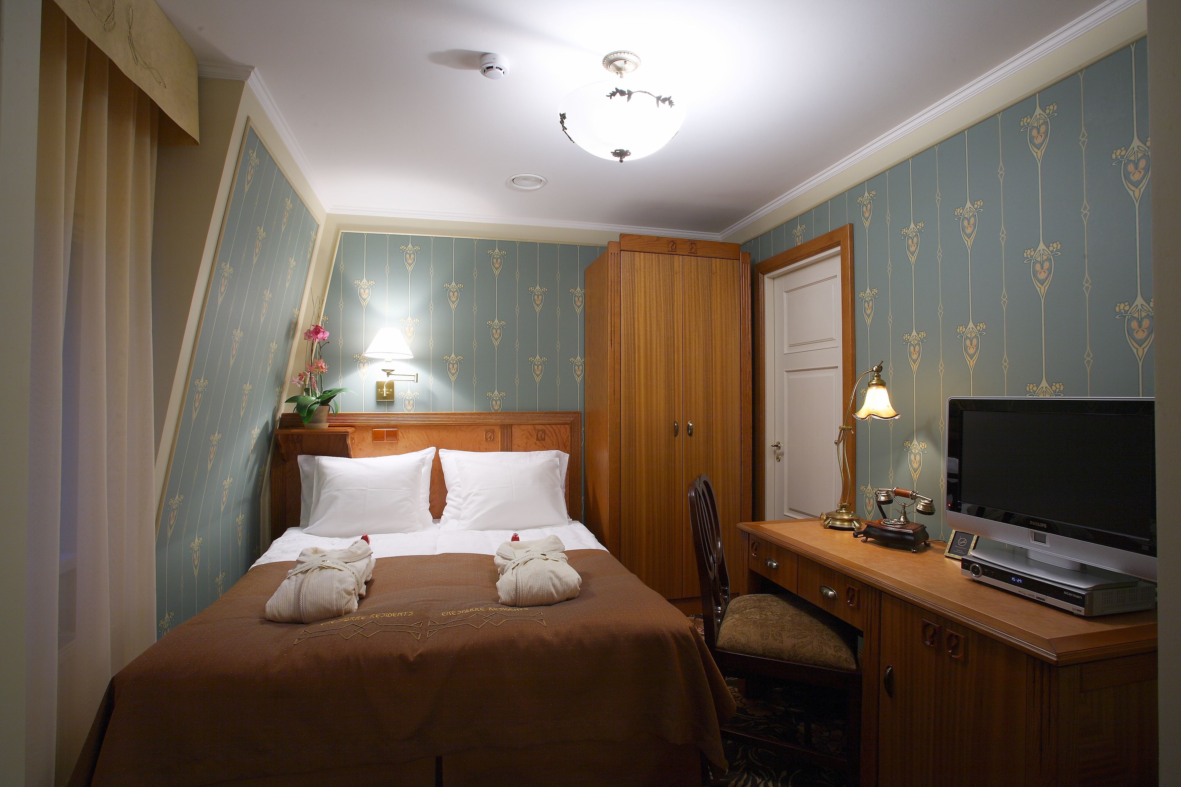 A hotel room with a bed, a desk with a television, and a wooden wardrobe.
